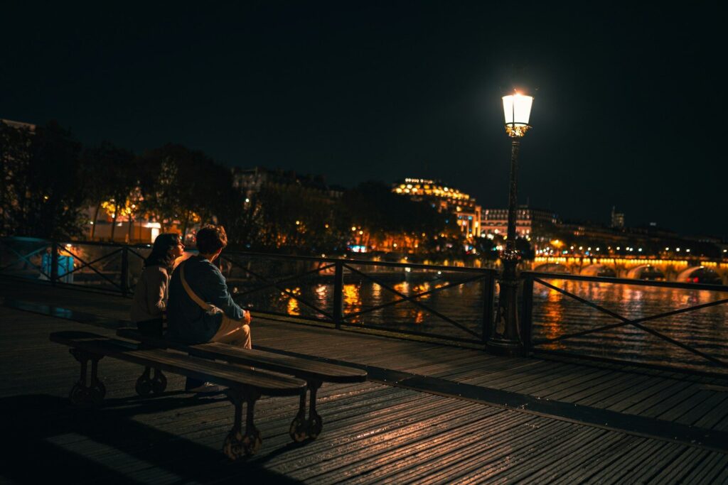 two people sitting on a bench next to a body of water